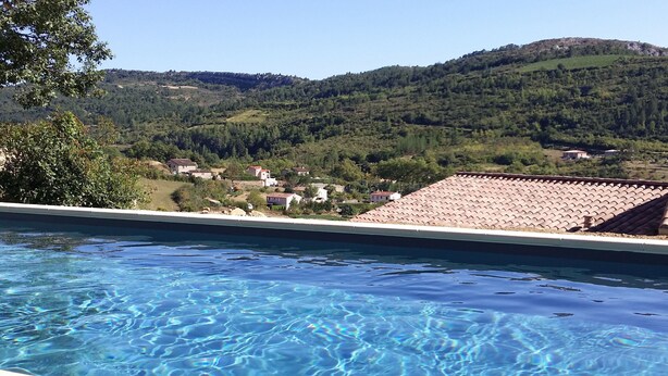 Una piscina con agua cristalina, rodeada por una colina con casas y árboles.