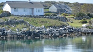 A coastal house with a stone wall and a grassy hill in the background.