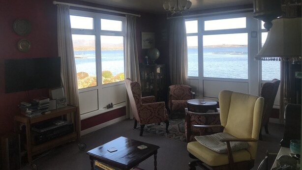 A living room with a view of the sea, a chandelier, and a television on a stand.