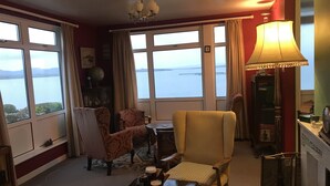 A cozy living room with a view of the sea, a table with drinks, and a lamp.