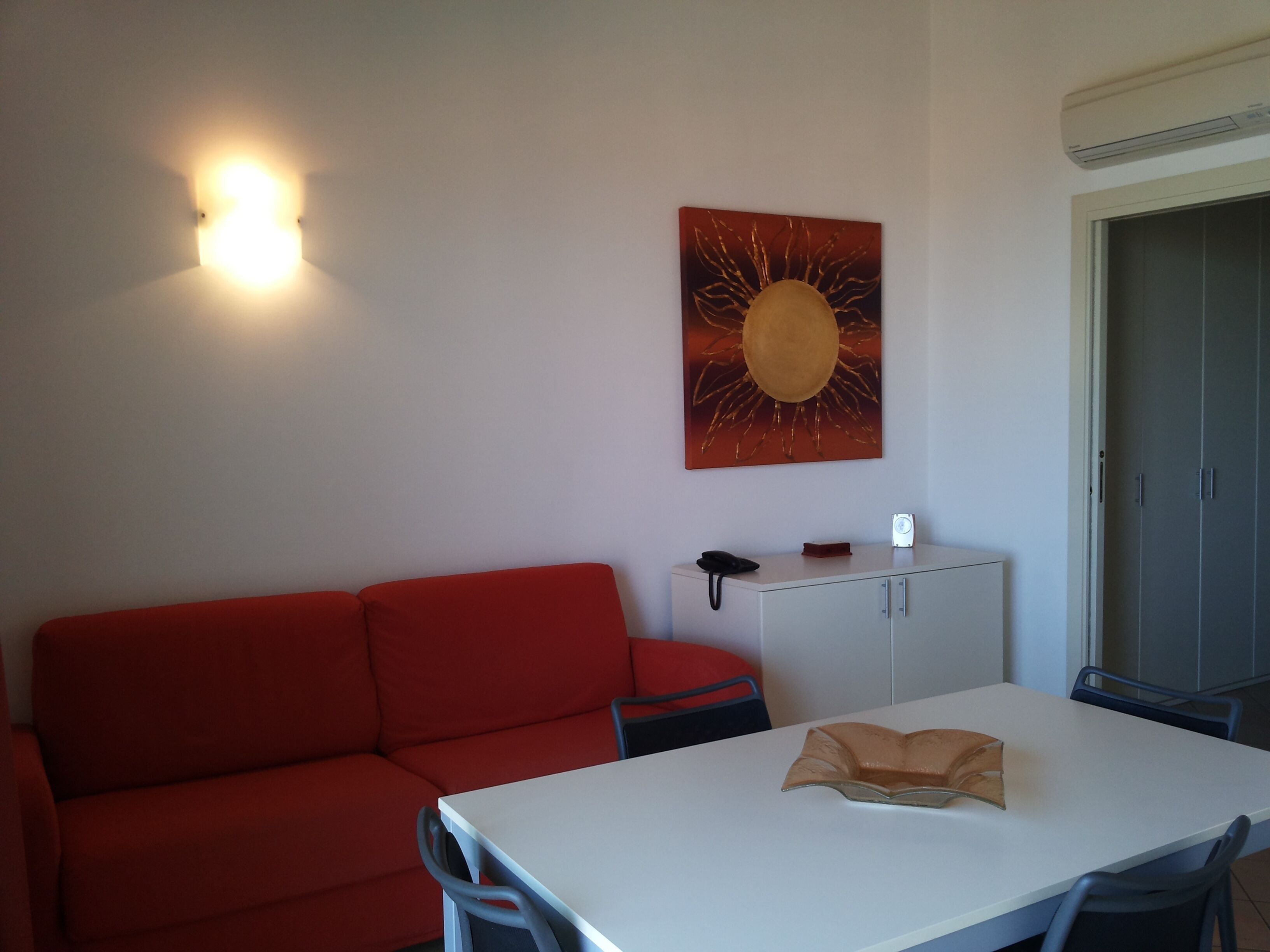 A room with a red sofa, a white table with a brown object, a cabinet, and a wall-mounted light fixture.