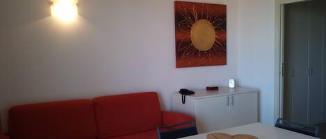 A room with a red sofa, a white table with a brown object, a cabinet, and a wall-mounted light fixture.