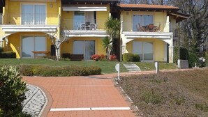 A two-story building with a yellow facade, balconies, and a paved driveway. - Stunning three-room lake view in a residence with three swimming pools and 36,000 m2 of greenery (Manerba del Garda)