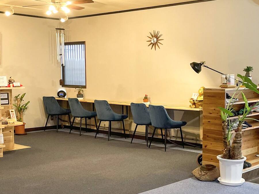 Een receptiebalie met een houten bureau, blauwe stoelen, een klok, een ingelijste schilderij en een potplant.