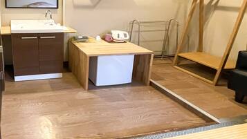 A compact kitchen with a sink, cabinets, a small refrigerator, and a wooden table with a kettle and cups.