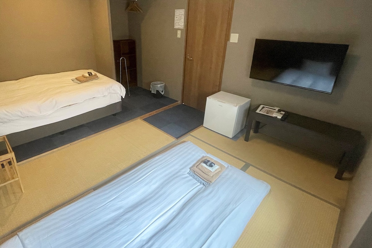 A hotel room with two beds, a small desk, a television, and a refrigerator.