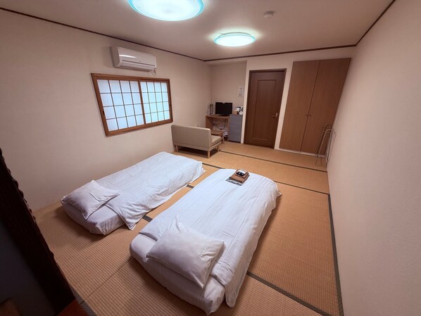 A hotel room with two beds, a futon, a television, and a wardrobe. - Reimeien (Osaka)