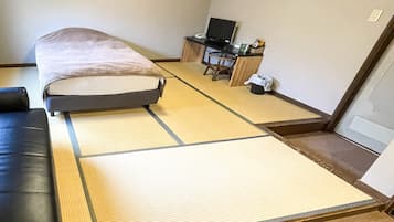 A room with tatami mats, a bed, a black leather sofa, a desk with a computer, and a chair.
