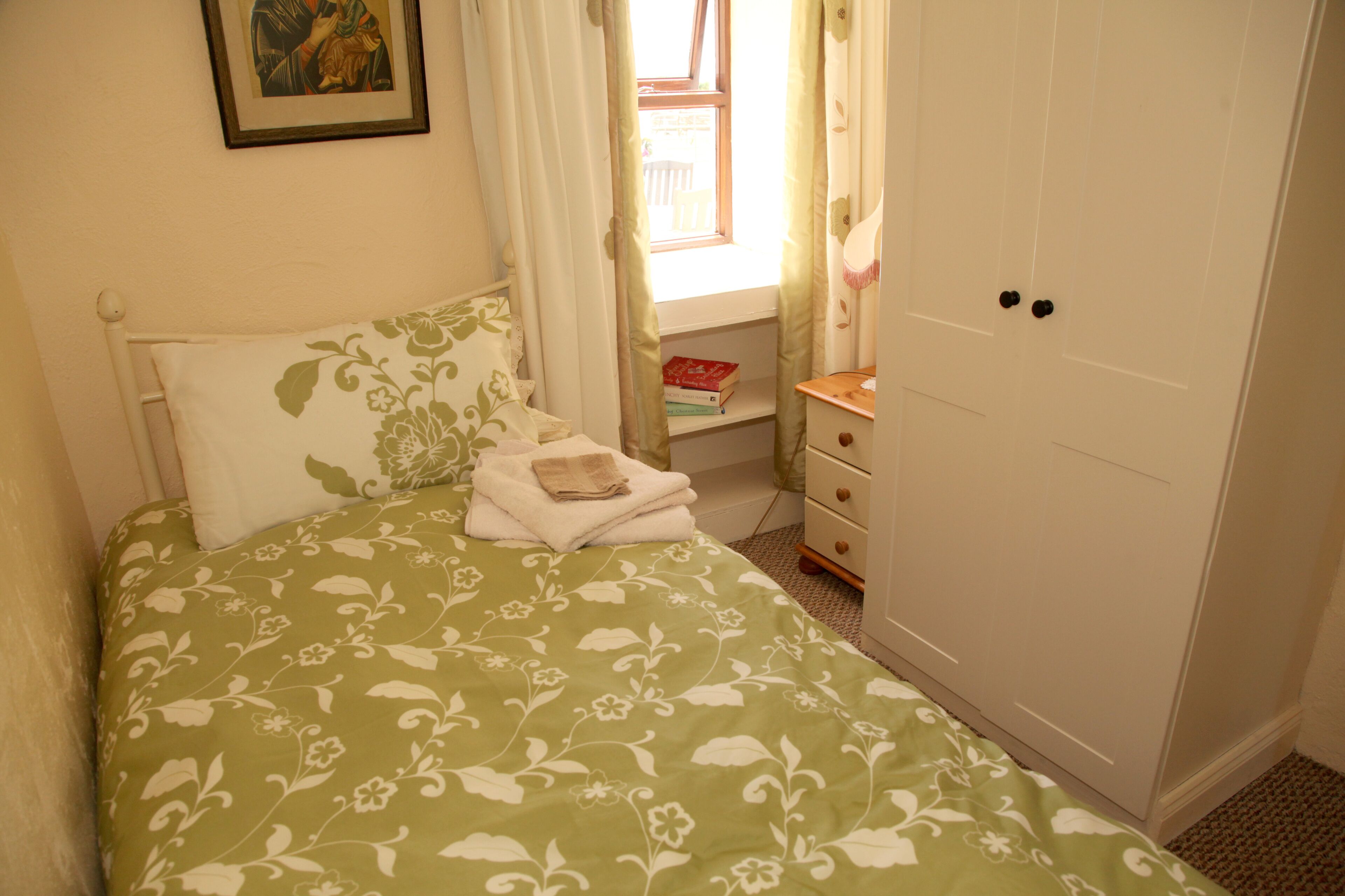 Een slaapkamer met een bed, een dressoir, een raam met gordijnen en een ingelijst schilderij aan de muur.