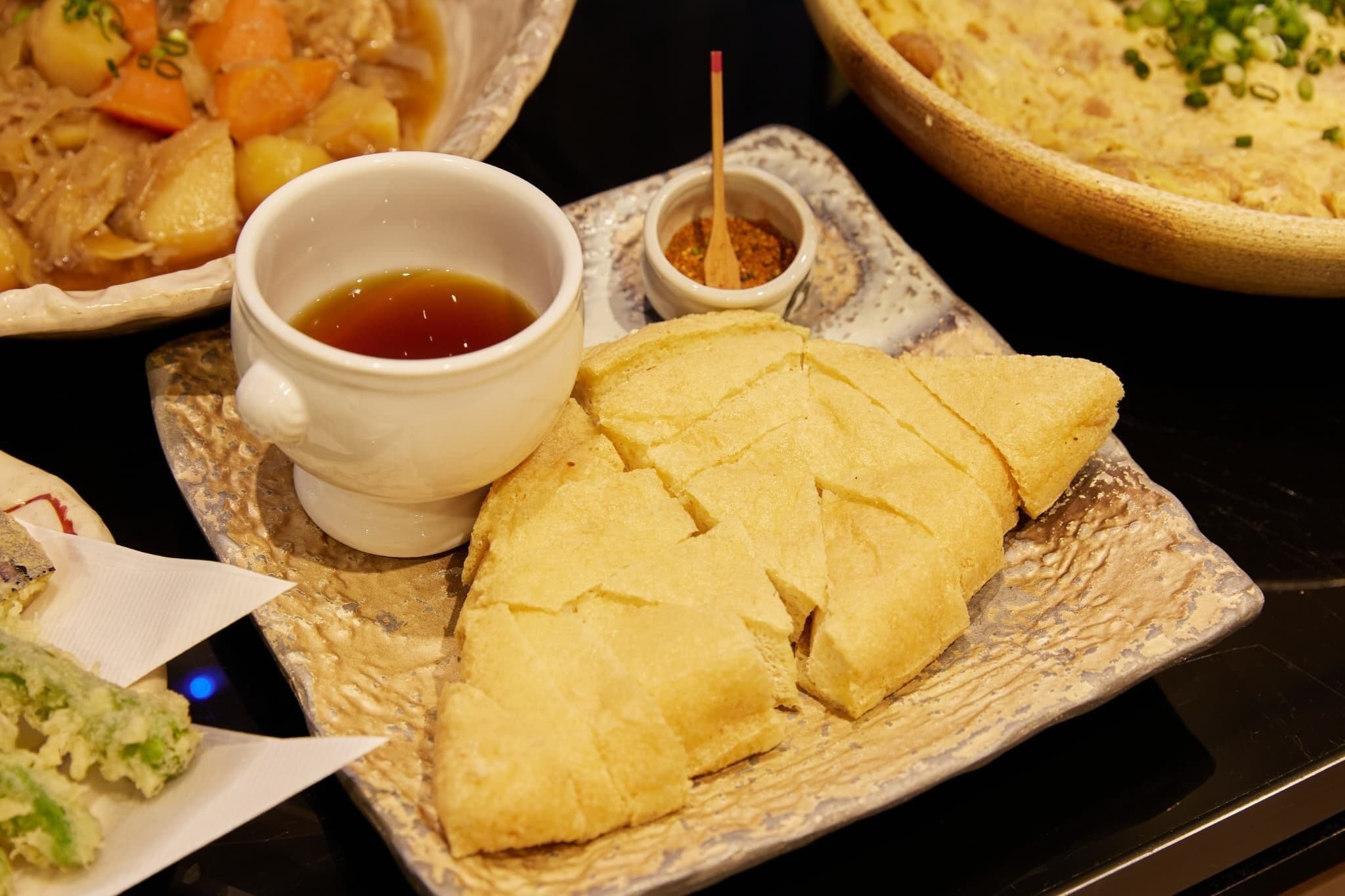 A meal with a bowl of soup, a piece of bread, and a small dish of sauce on a table.