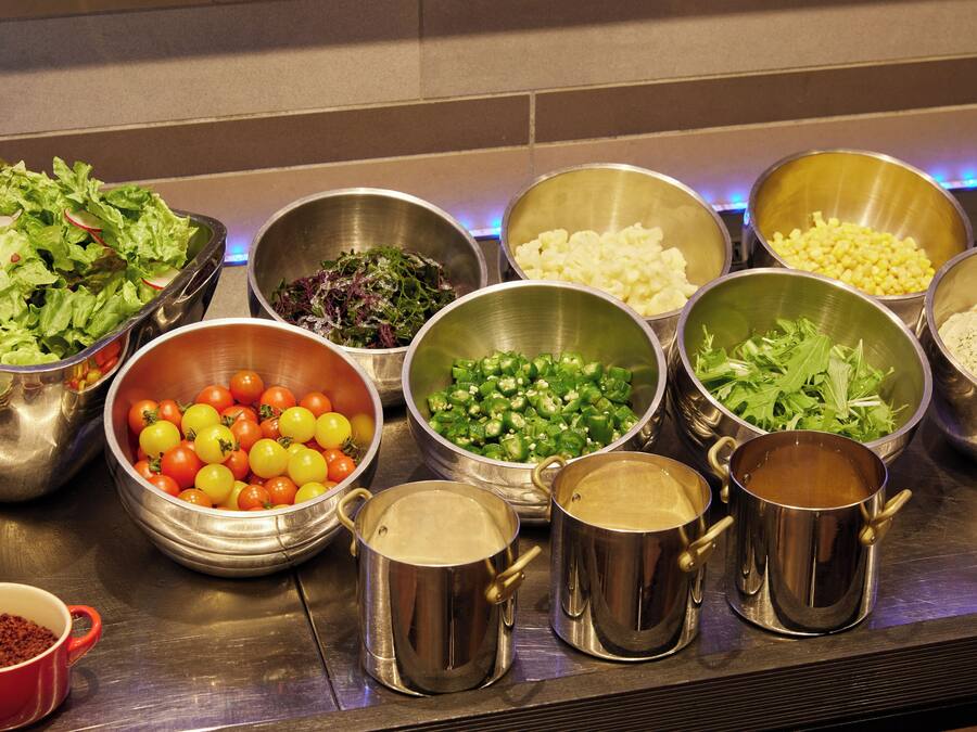 Ein Buffet mit verschiedenen Speisen in Metallschüsseln und -töpfen, darunter Salate, Gemüse und weitere Gerichte.