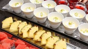 A tray with sliced pineapple and watermelon, and small bowls with a creamy dessert topped with green garnish.