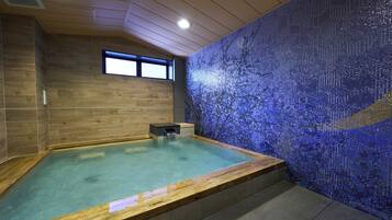 A modern spa room with a wooden floor, a large bathtub, and a mosaic wall.