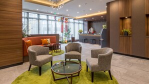 A modern lobby with a sofa, armchairs, a glass table, and a reception desk. - Almont Hotel Sendai (Sendai)