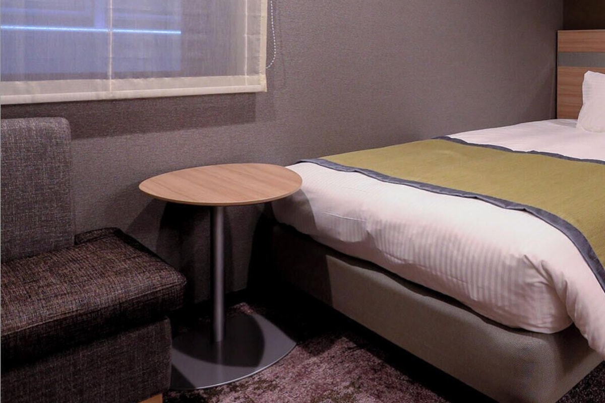 A hotel room with a bed, a round table, a chair, and a window with a curtain.