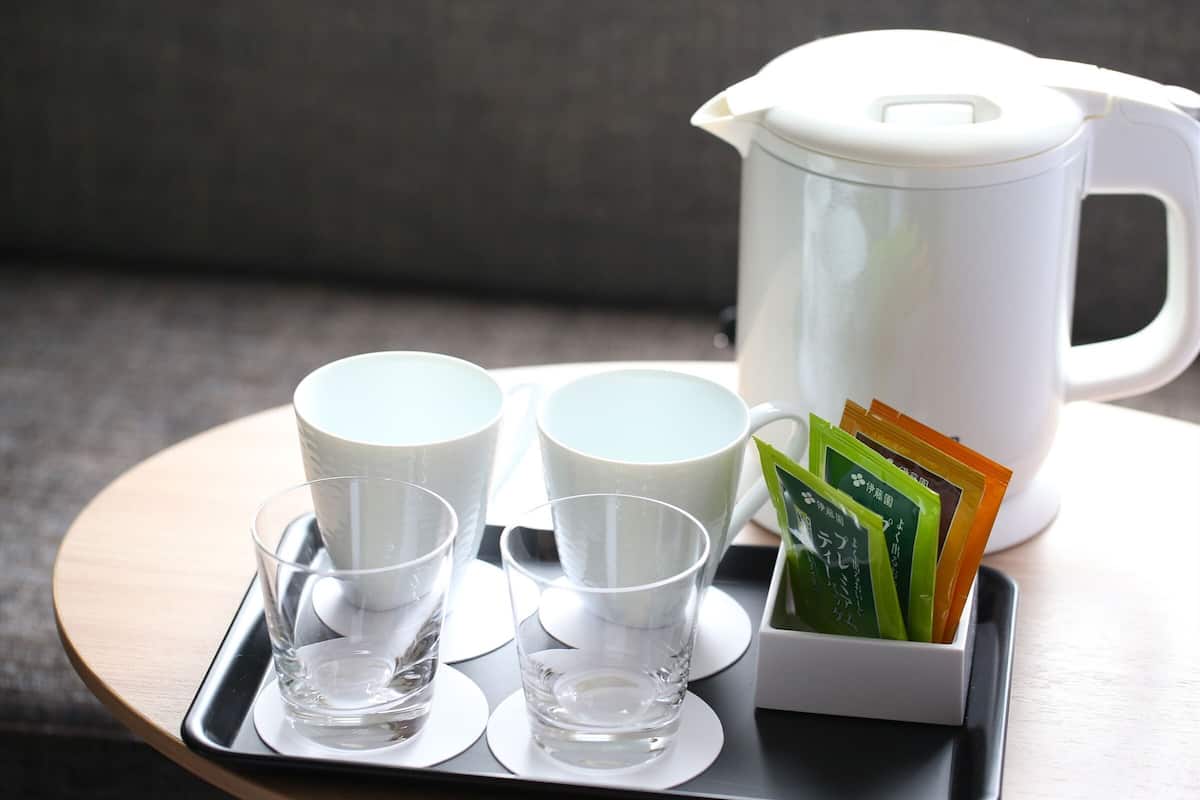 A tray with two cups, a glass, and a tea kettle with tea bags.