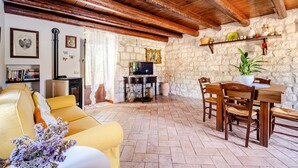 A cozy living room with a sofa, a dining table with chairs, a television, and a stone wall.