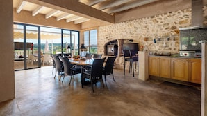 A spacious kitchen with a stone wall, a large dining table, and a view through glass doors.