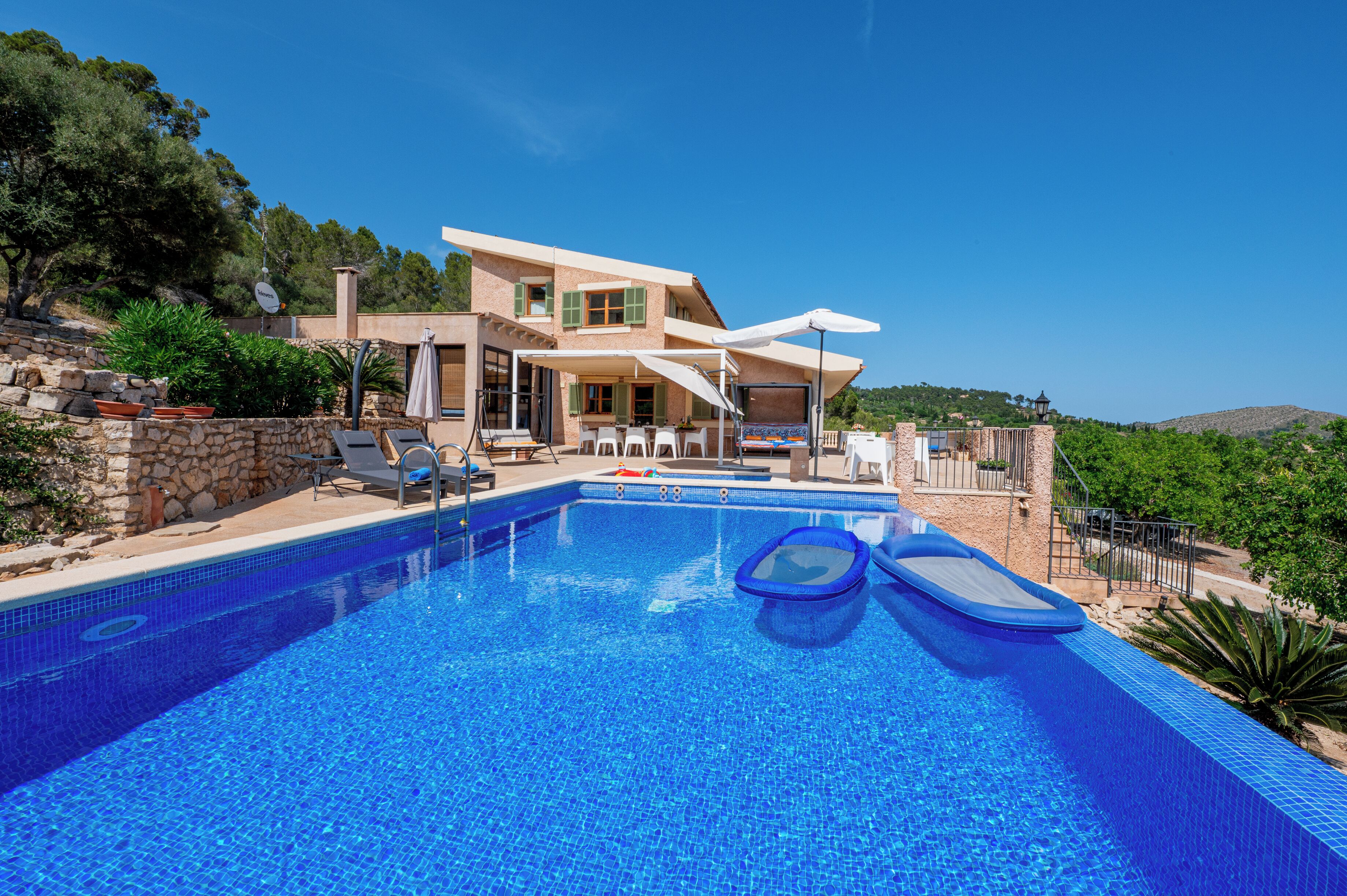 A modern villa with a swimming pool, outdoor seating, and a view of the surrounding landscape.