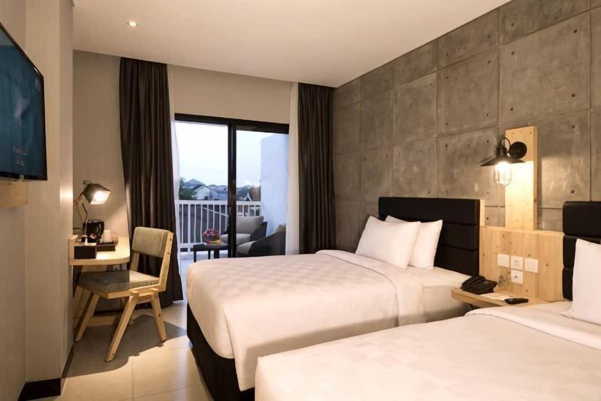 Habitación de hotel con dos camas, un escritorio, una silla, un televisor y un balcón con cortinas.