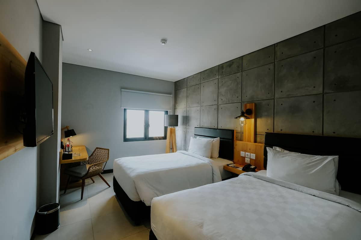 Habitación de hotel con dos camas, un escritorio, una silla y un televisor.