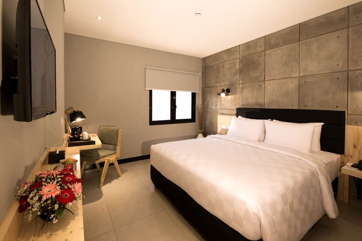 Una habitación de hotel moderna con una cama grande, un escritorio con una silla, un televisor de pantalla plana y una lámpara de pared.