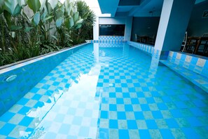 Ein Swimmingpool mit blau-karierten Fliesen, umgeben von Pflanzen und einem modernen Gebäudebau.
