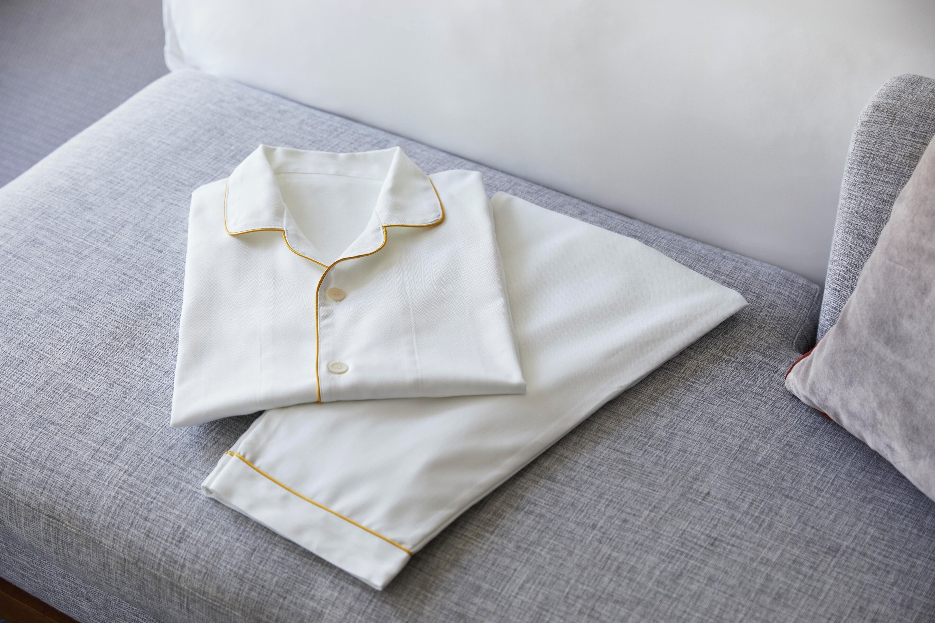 A neatly folded white shirt with gold trim on a gray sofa.