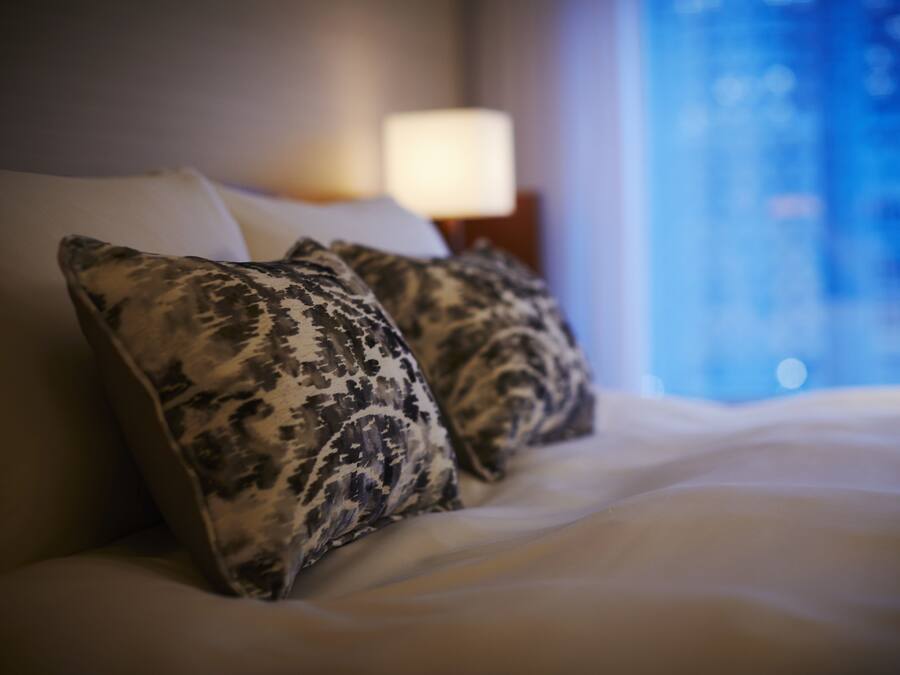 A bed with patterned pillows and a view of a cityscape through a window.