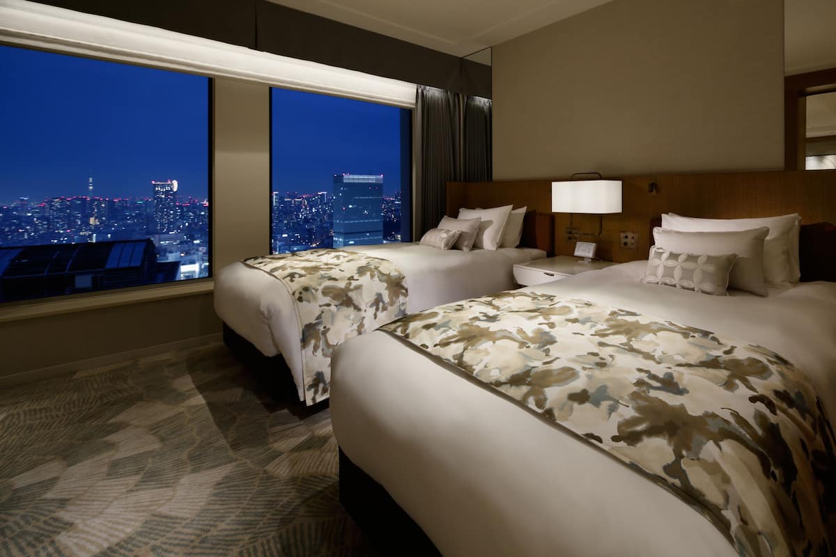 Habitación de hotel con dos camas, vista a la ciudad, un ventanal grande y piso alfombrado.
