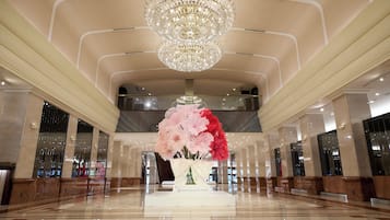 A spacious lobby with a large chandelier, a central floral arrangement, and a polished marble floor.