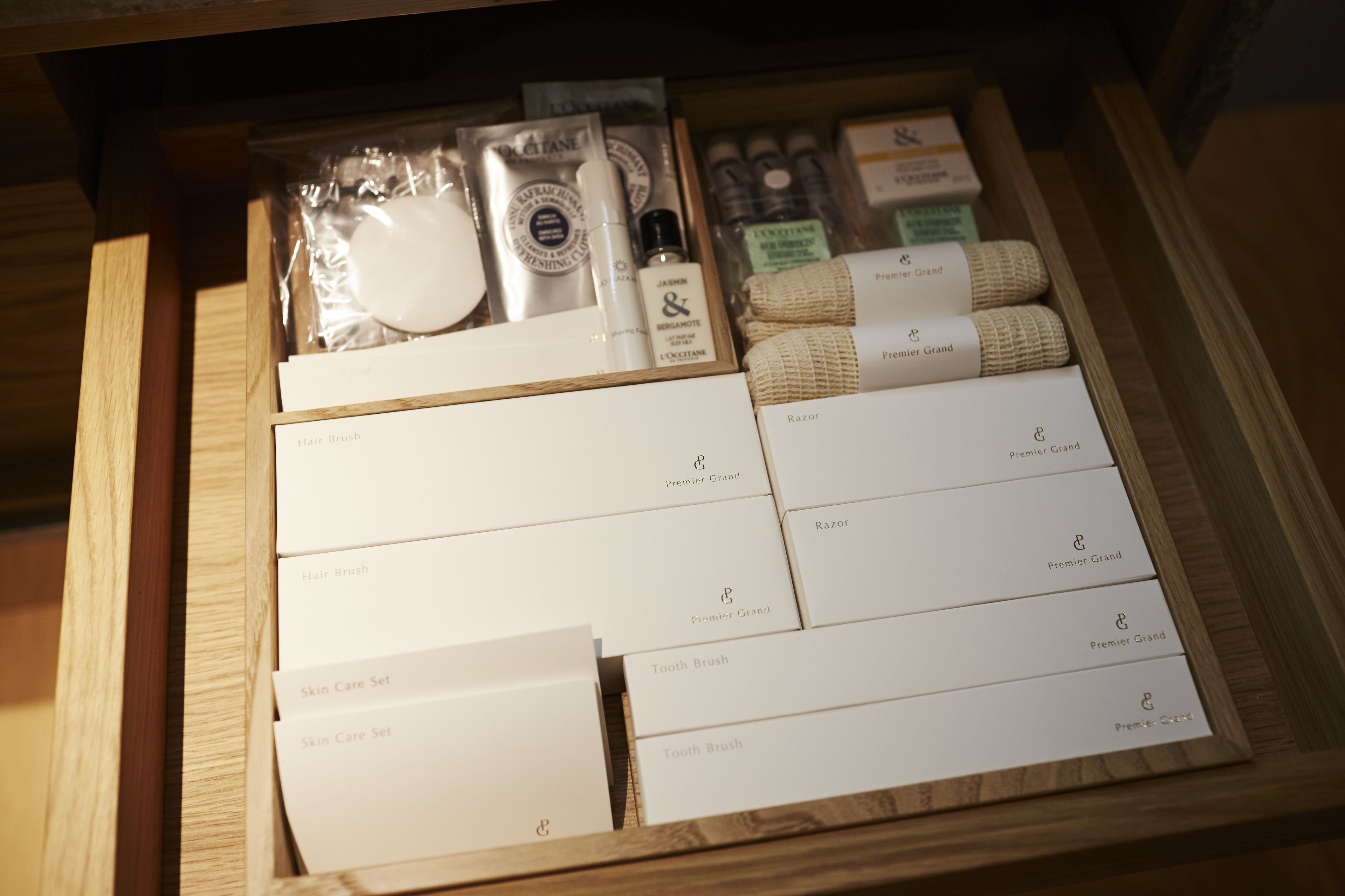 A drawer containing various personal care items including hairbrushes, razors, and toothbrushes, all branded by Premier Grand.