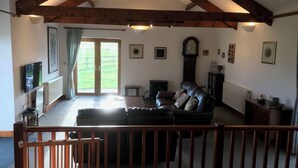 A spacious living room with a leather sofa, a wooden coffee table, and a large clock on the wall. - Large Detached "upside Down" Barn, dog friendly with 1 acre enclosed paddock. (wellington)