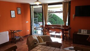 Une pièce aux murs orange, un coin repas avec des chaises et une table, un lit recouvert d’une couverture à carreaux, un radiateur et un téléviseur fixé au mur.