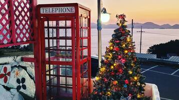 A red telephone booth with a sign, a decorated Christmas tree, and a view of the sea.