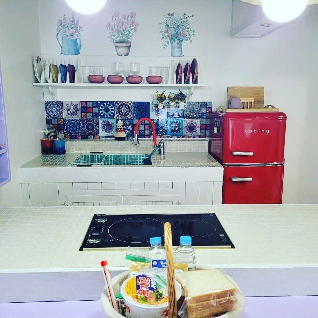 A kitchen with a white countertop, a red refrigerator, and a backsplash with colorful tiles.
