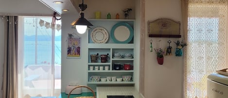 A kitchen with a green table, a sink, and a refrigerator. There are shelves with dishes and a hanging plant.
