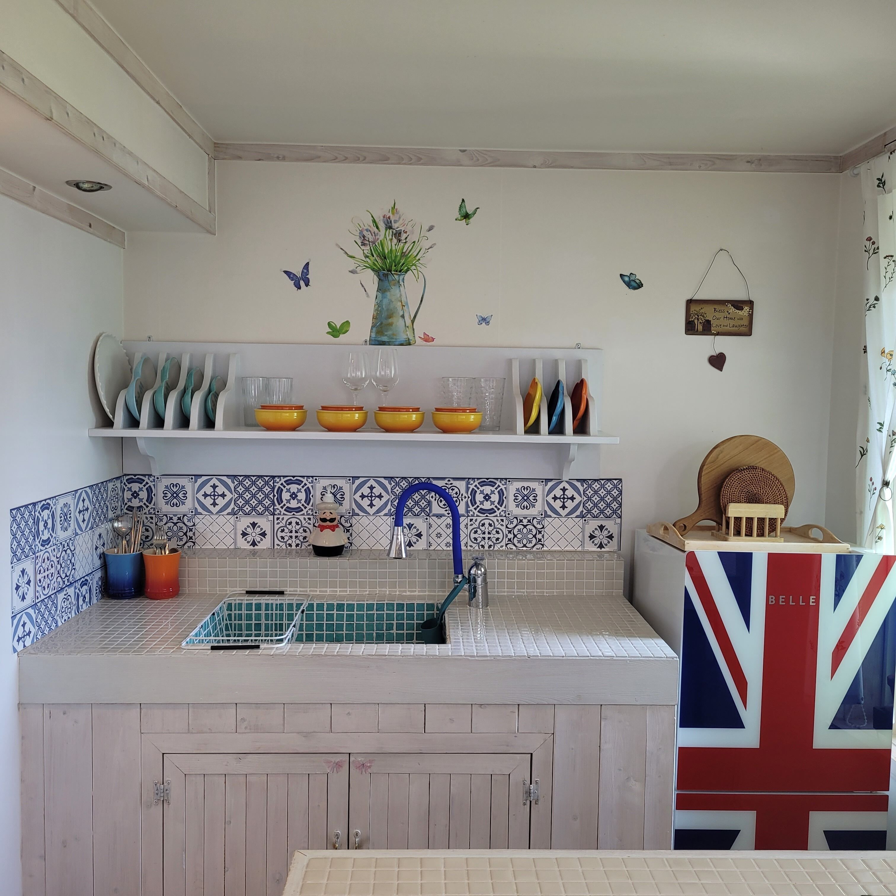 A kitchen with a sink, a decorative wall with butterfly decals, and a shelf with bowls and glasses.