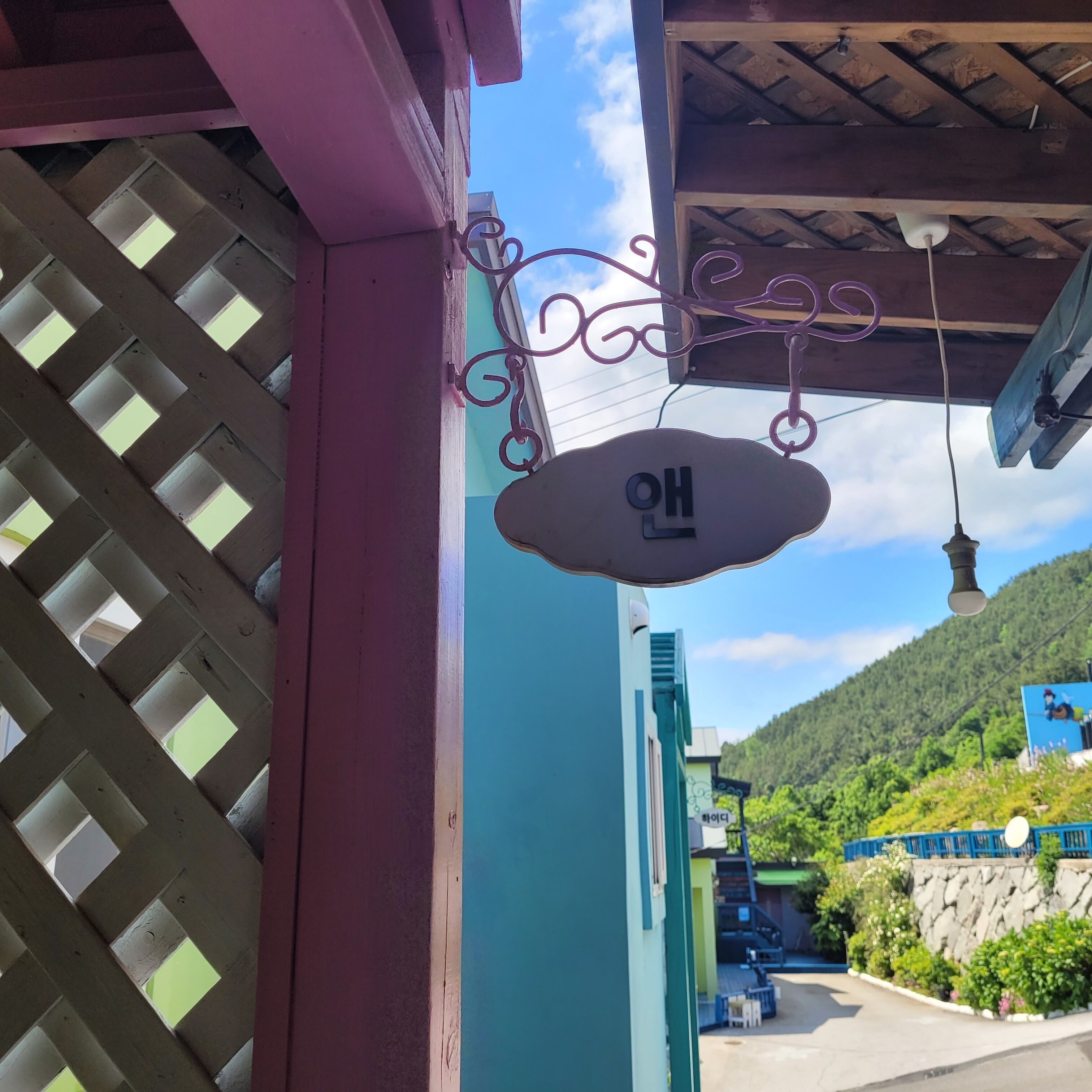 Um edifício com janela treliçada, uma placa suspensa com caracteres coreanos e vista para uma colina verde.