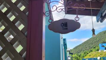 Um edifício com janela treliçada, uma placa suspensa com caracteres coreanos e vista para uma colina verde.