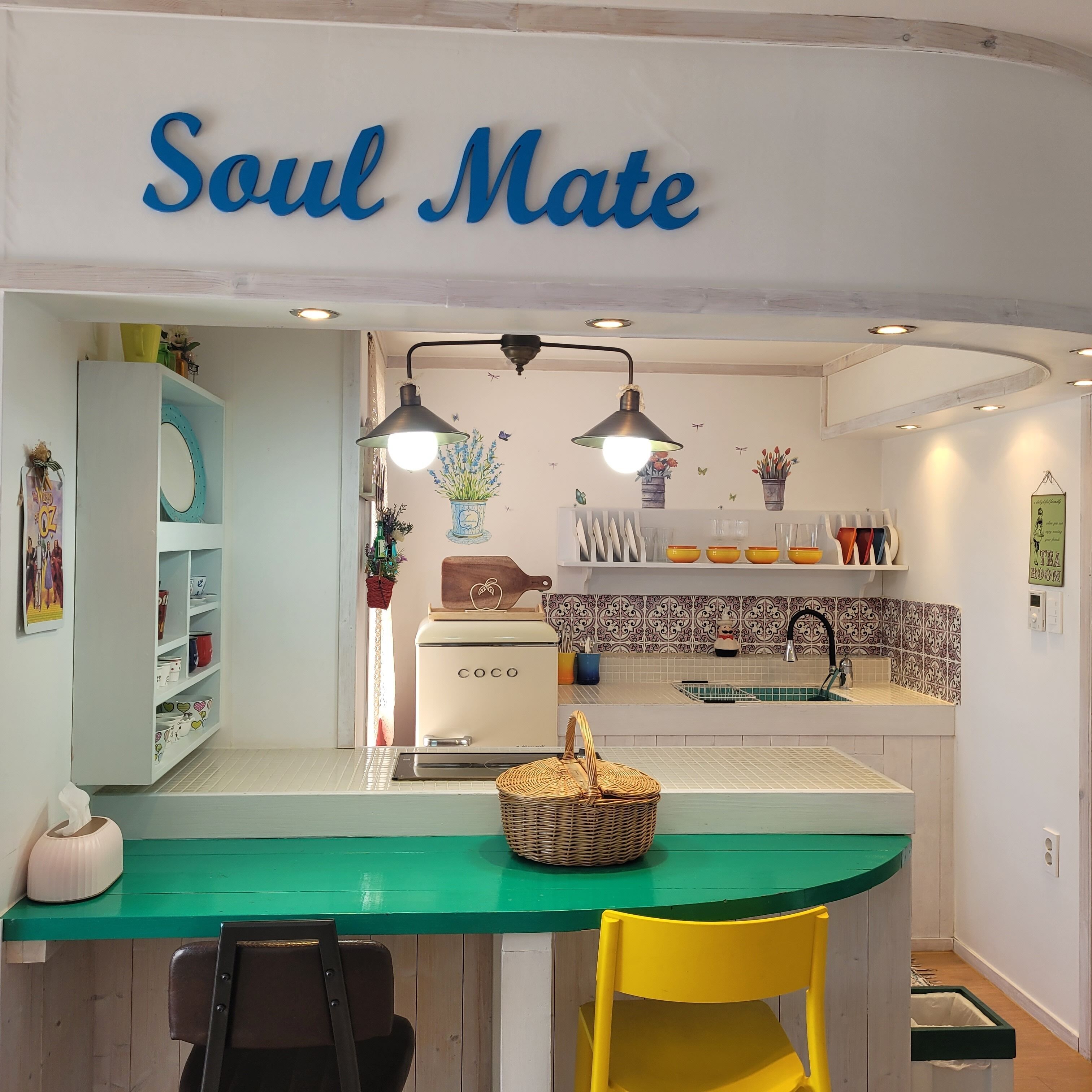 Een keuken met een groen aanrecht, een gele stoel, een witte koelkast en een bord dat "Soul Mate" zegt.