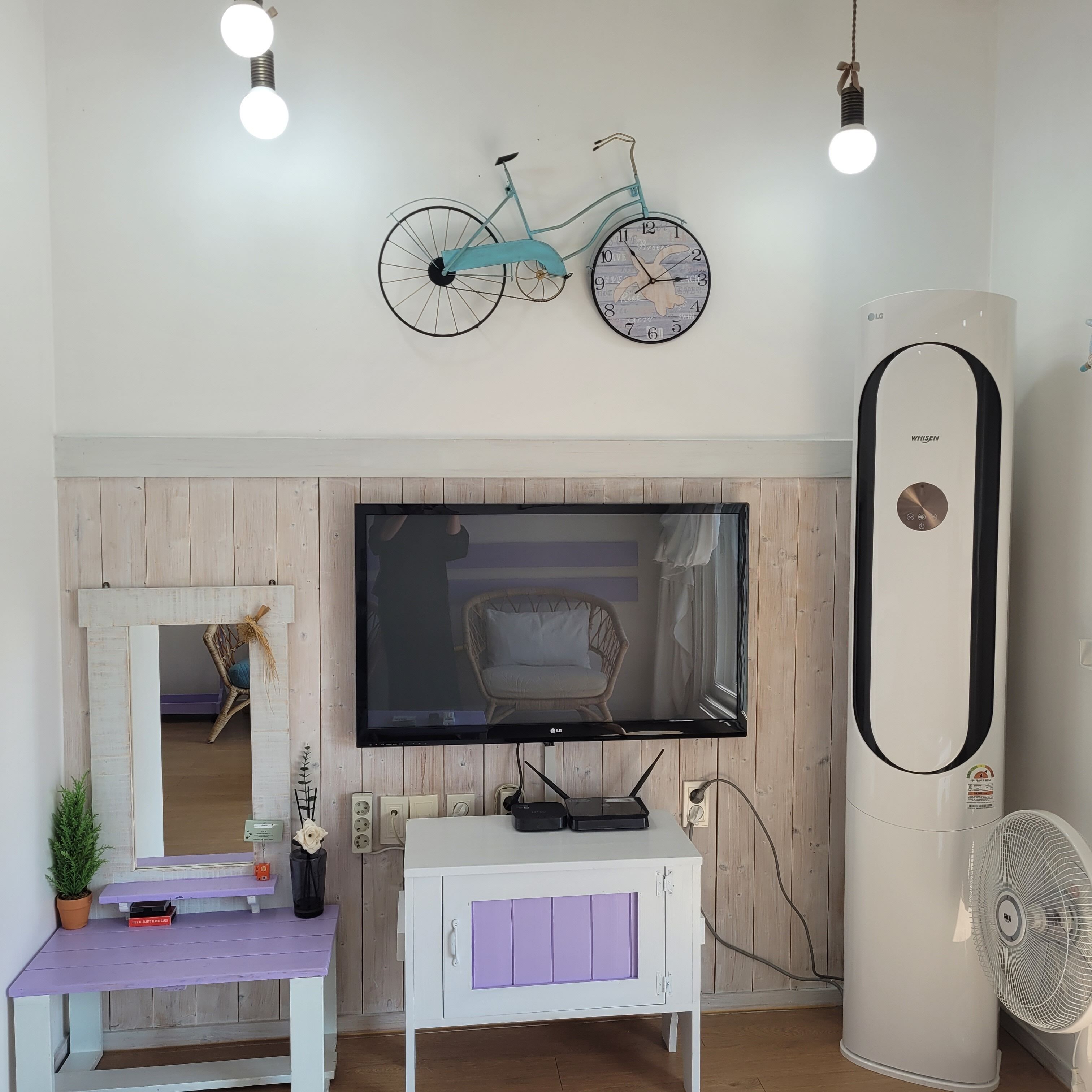 Sala de estar com televisão na parede, ar condicionado branco e relógio de bicicleta fixado na parede.