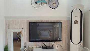 Sala de estar com televisão na parede, ar condicionado branco e relógio de bicicleta fixado na parede.