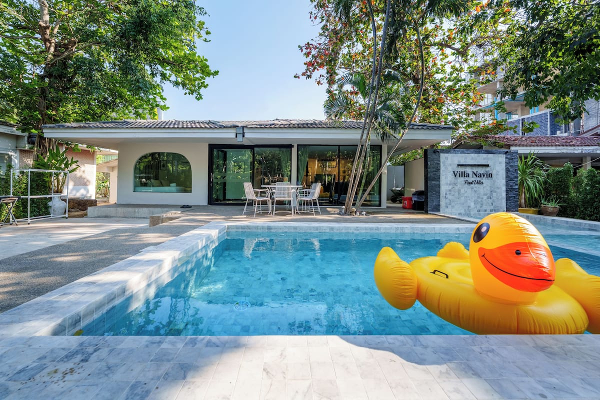 A swimming pool with a yellow inflatable duck, a patio with a table and chairs, and a villa named "Villa Navin."