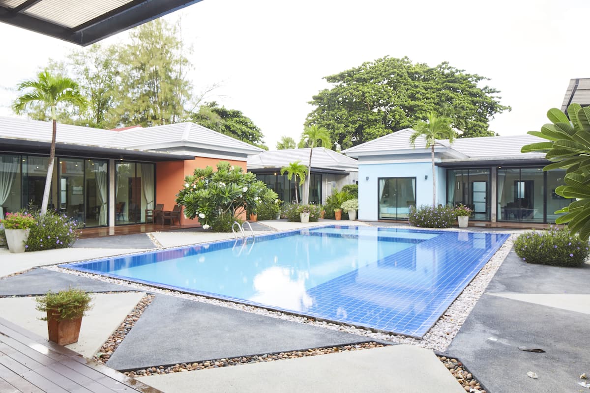 A swimming pool with a tiled edge, surrounded by a deck with potted plants and a palm tree.