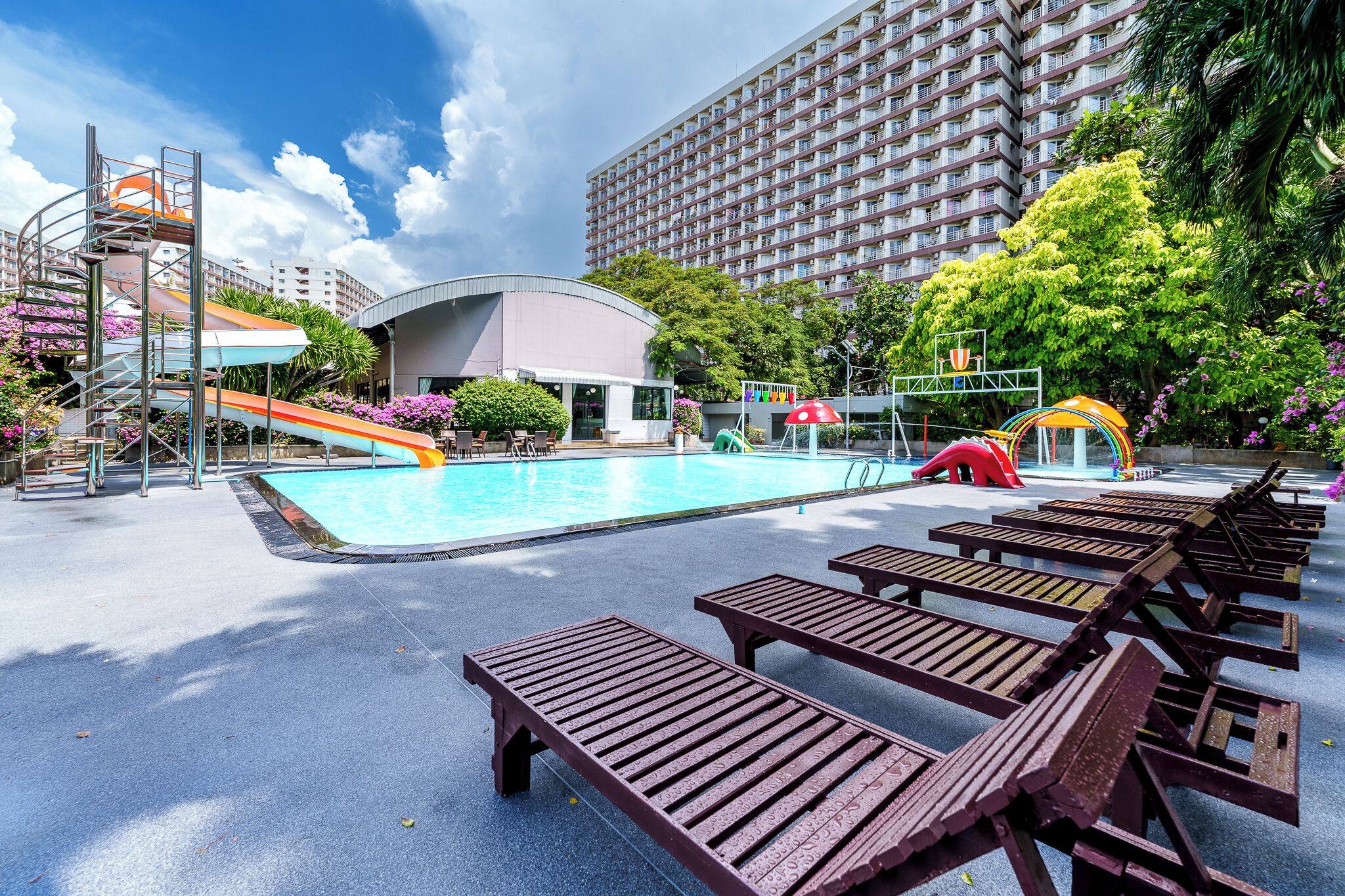 Una piscina con toboganes, sillas de descanso y un edificio al fondo.