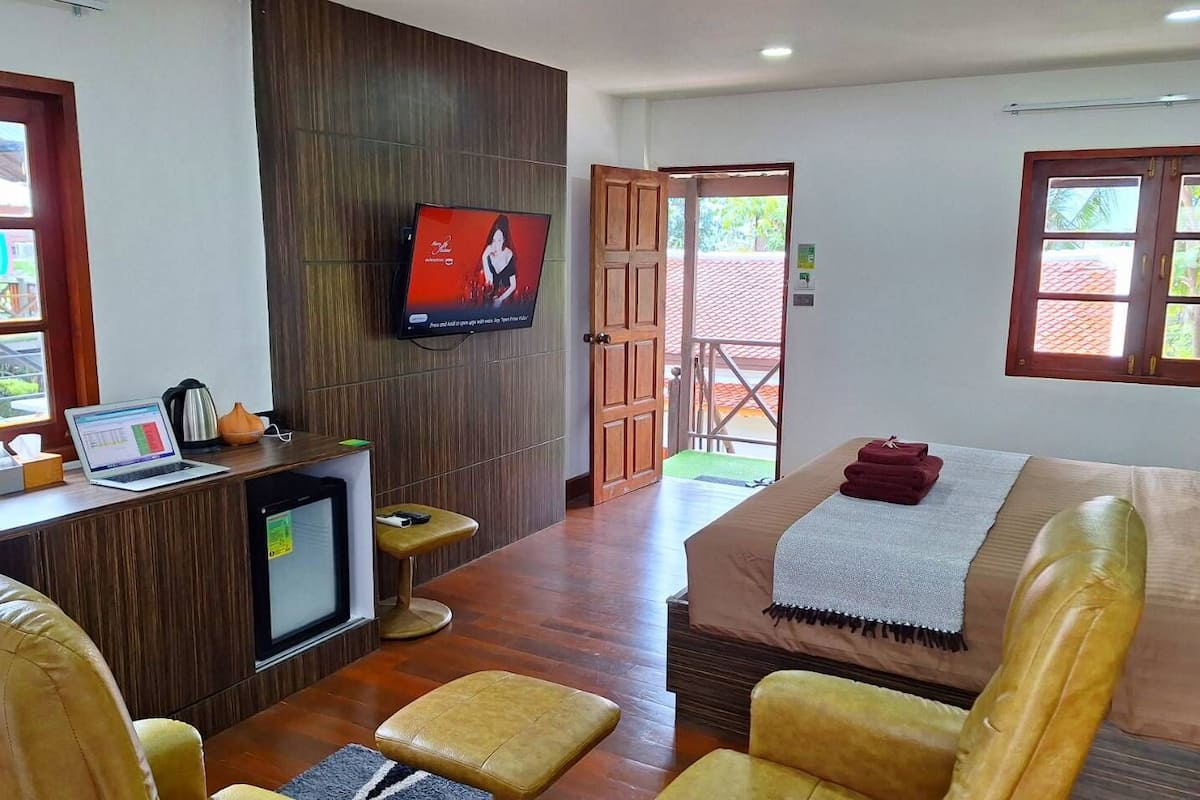 A hotel room with a wooden desk, a television, a bed with a red blanket, and a view of the outside.