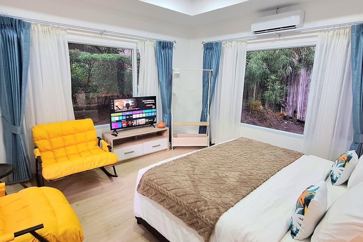 A hotel room with a bed, a TV, a chair, and a window with a view of trees.