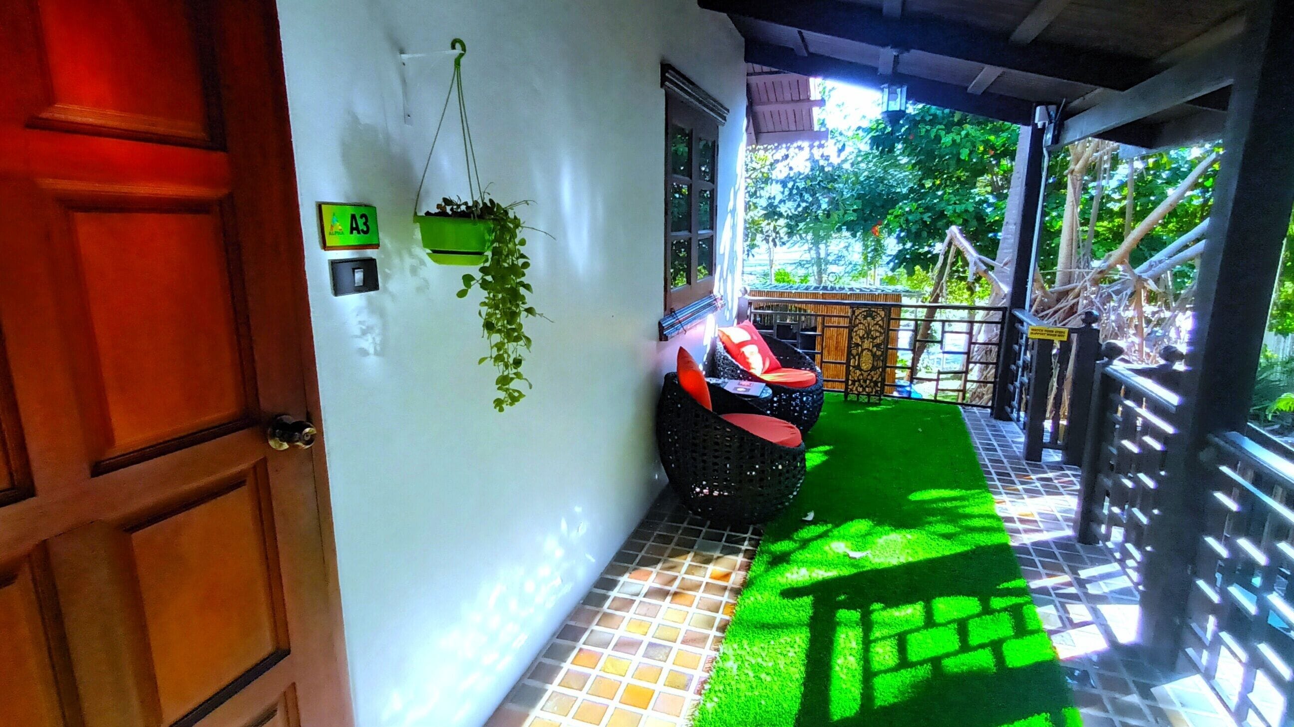 A hallway with a green artificial grass area, a black wicker chair with red cushions, and a hanging plant.