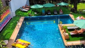 A swimming pool with a clear blue water, surrounded by green artificial grass, and equipped with lounge chairs and umbrellas.